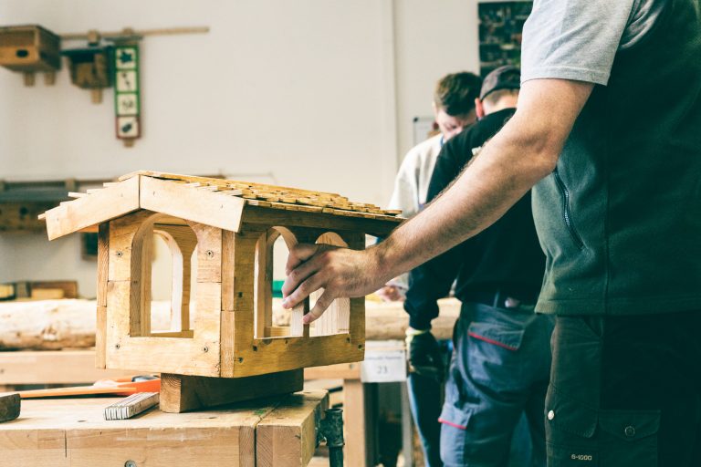 Detailaufnahme. Eine Hand hält ein aus Holz gefertigtes Vogelfutterhaus. Holzwerkstatt im Kommunalen Eigenbetrieb Leipzig / Engelsdorf.