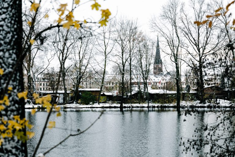 Der Ullrichteich an der Villa KAOS im Lindenauer Stadtgarten, Leipzig. Im Hintergrund sieht man die Nathanelkirche in Lindenau. Es liegt eine leichte Schneedecke.
