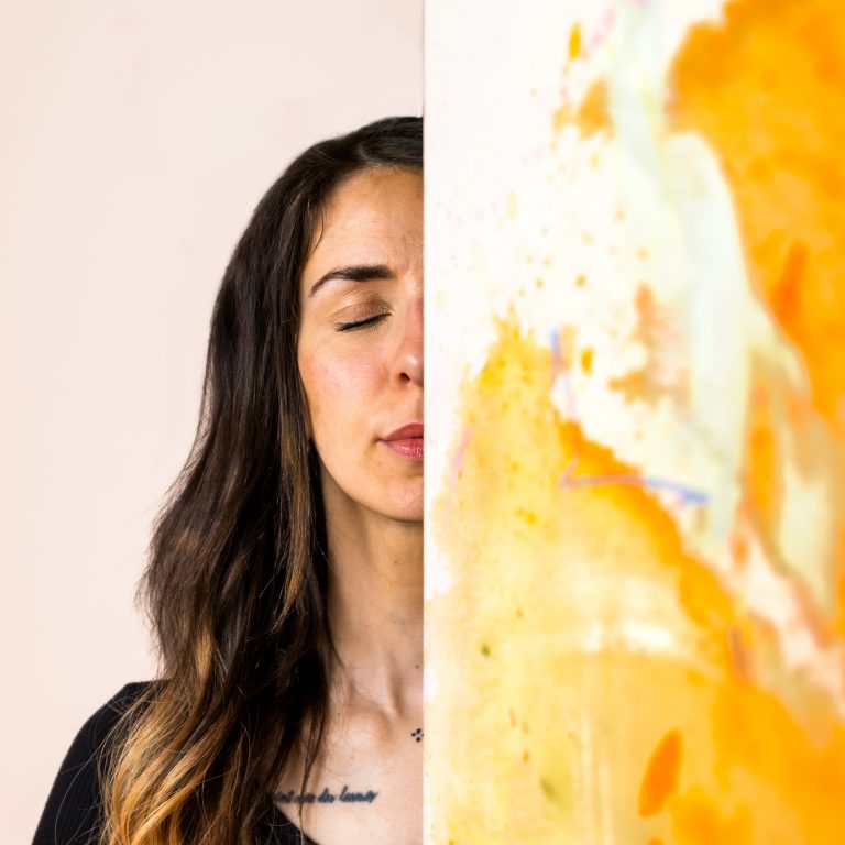 Portrait in Farbe. Es ist die Hälfte des Gesichts einer Künstlerin zu sehen. Ihr Auge ist geschlossen. Die andere Gesichtshälfte wird von einem Gemälde verdeckt.