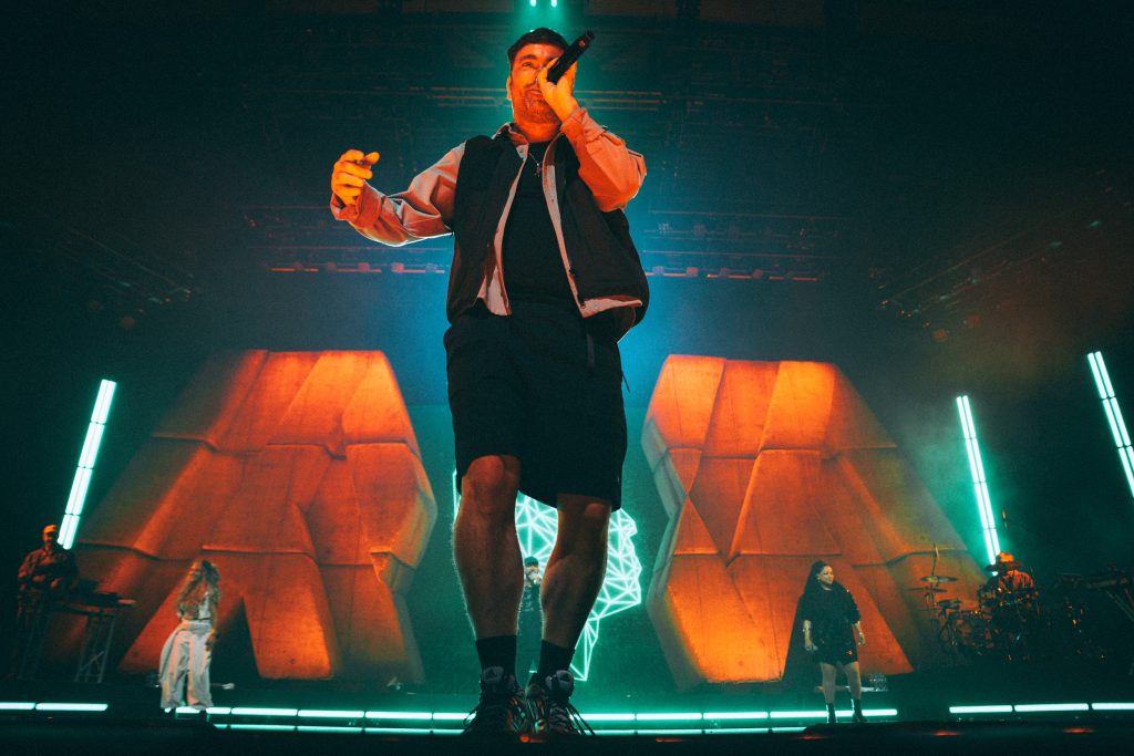 Marteria live in der Quarterback Immobilien Arena Leipzig: Weitwinkelblick auf die Bühne mit orangefarbenen Aufbauten, türkisen Lichtstäben und Band