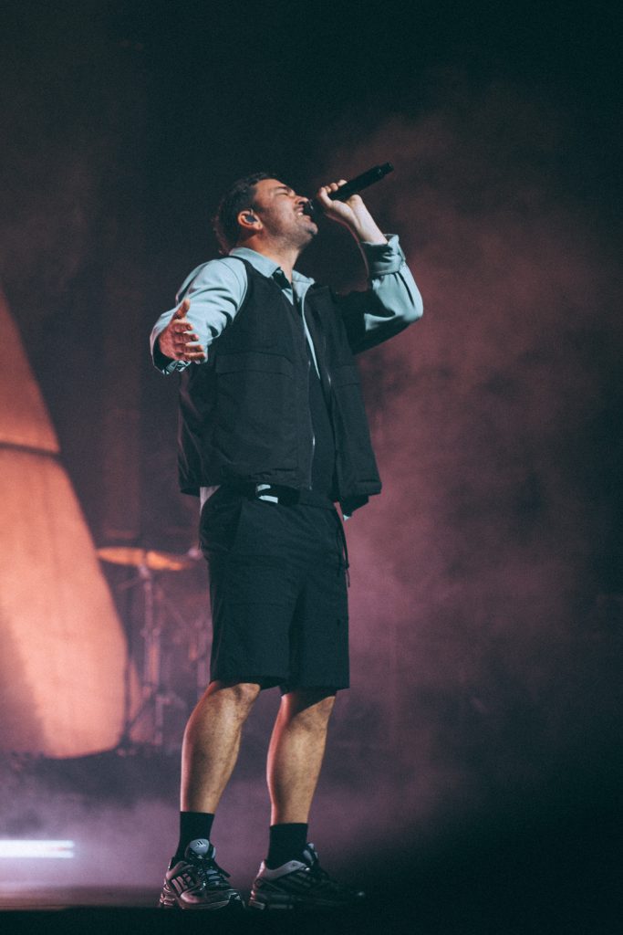 Concert photography Leipzig: Marteria mit erhobener Faust und Mikrofon vor rosa-orangefarbenem Bühnennebel