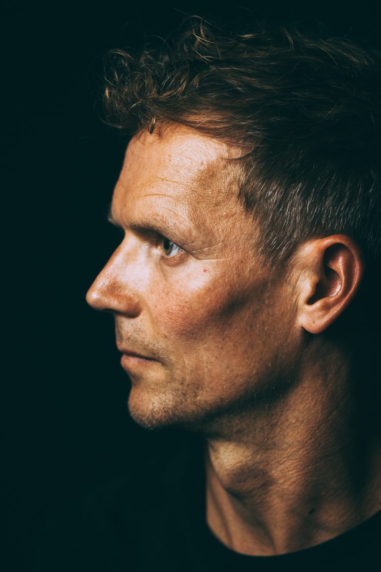 Nahbares Portrait im Profil, Mann mit nachdenklichem Ausdruck, schwarzer Hintergrund, Portraitshooting in Leipzig